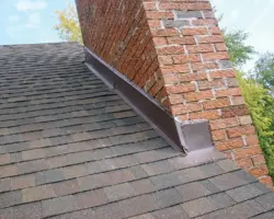 Close-up exterior view of brown asphalt shingle roofing with newly installed metal step flashing and counter flashing fitted against a red brick chimney stack.