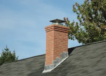 Close-up of a brick chimney stack fitted with a metal cowl and cap against a clear blue sky.