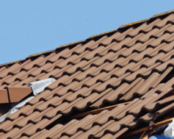 Close-up of a brown interlocking tiled roof showing damaged and missing sections undergoing professional roof repair.