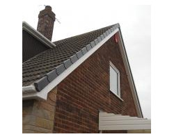 Exterior view of a red brick house gable featuring a grey dry verge roof system, white uPVC fascias, and a traditional brick chimney stack