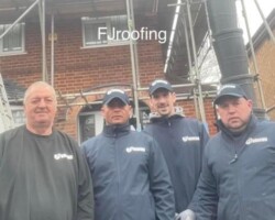 Professional team of roofing contractors and builders standing in front of scaffolding and a brick house.