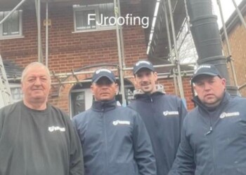 Professional team of roofing contractors and builders standing in front of scaffolding and a brick house.