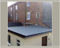 Elevated view of a modern flat roof extension with grey waterproofing membrane, set against multi-story red brick residential buildings.