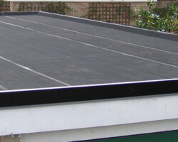 Elevated exterior view of a flat roof finished with black mineral felt waterproofing, neat edge trims, and white fascias above a brick wall.