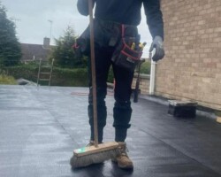 Text: Professional roofer sweeping and cleaning a newly installed flat felt roof on a residential property