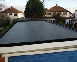 Elevated exterior view of a newly finished flat roof featuring a dark waterproofing membrane, clean white fascias, and surrounding residential properties.
