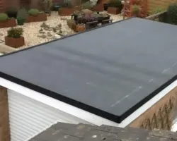 Elevated view of a newly waterproofed dark flat roof on a brick garage, featuring white fascias and overlooking a landscaped back garden with raised planters.