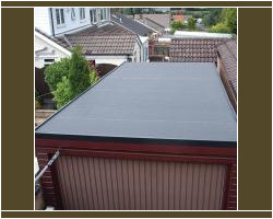 Elevated view of a newly installed dark grey waterproofing membrane on a residential garage flat roof set against neighboring houses.