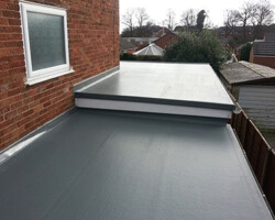 Elevated exterior view of a multi-level flat roof finished with a smooth grey waterproofing membrane, metal flashing against a brick wall, and white fascias.