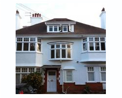 Front view of a large white rendered detached house featuring multiple bay windows, a central dormer roof window, and multiple white chimneys.