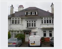 Front view of a large white rendered detached house with multiple chimneys, a dormer window, bay windows, and vehicles parked in the driveway.