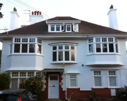 Exterior view of a large detached two-storey white rendered house with multiple bay windows, dormer roof window, and twin chimneys