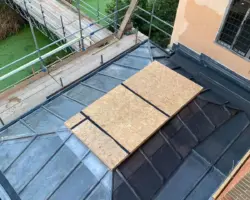 Overhead view of a lead-covered flat and pitched roof with a central skylight opening and surrounding scaffolding.