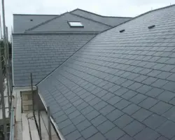 Elevated exterior view of a large pitched roof covered in grey slate tiles, featuring integrated skylights and adjacent scaffolding during construction.