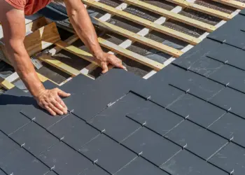 Professional roofer carefully laying and securing dark roof tiles onto wooden battens and membrane during installation