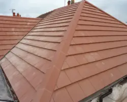 Elevated view of a newly installed red clay hip roof with precision-fitted hip tiles and clean ridge lines against an overcast sky.