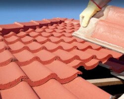 Close-up of a worker wearing protective gloves replacing or repairing red clay roof tiles on a sunny day.