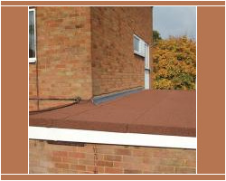 Elevated view of a red mineral felt flat roof with lead flashing against a brick wall and autumn trees in the background.