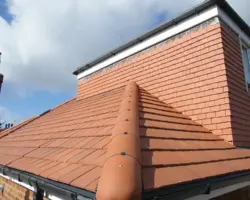 Exterior view of a red tile hip roof featuring a mechanical dry ridge system and matching red clay ridge tiles meeting a tiled extension wall.