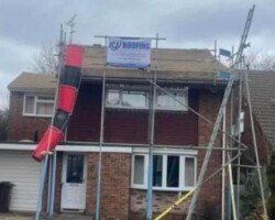 Two-story detached house featuring exterior scaffolding and a red debris chute installed for roof replacement