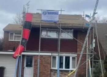Two-story detached house featuring exterior scaffolding and a red debris chute installed for roof replacement