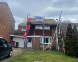 Residential house under renovation with exterior scaffolding and a debris chute setup by roofing contractors.