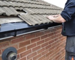 Close-up of a roofer repairing concrete roof tiles above a newly installed black uPVC gutter and brick wall.