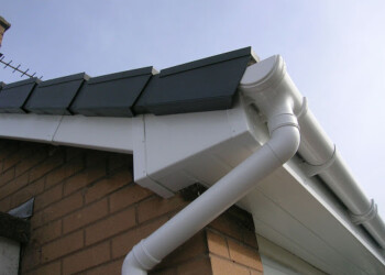 Newly installed white uPVC fascias, soffits, and guttering system on a brick residential roof with dark roof tiles.