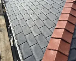 Elevated view of a dark slate roof finished with contrasting red clay ridge tiles, alongside exterior scaffolding.