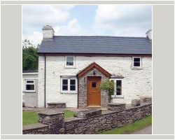 Front view of a traditional white painted stone cottage featuring a newly installed dark slate roof, dual chimneys, and a stone porch entrance.