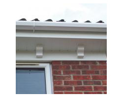 Close-up view of newly installed white uPVC fascias featuring decorative corbel brackets, clean guttering, and a brick exterior wall