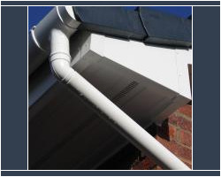 Close-up view of newly installed white uPVC fascias, ventilated soffits, guttering, and a downpipe on a residential brick roofline.