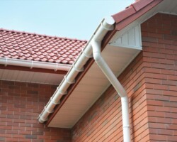 Close-up of white PVC guttering and downpipe installed on a red brick home with a red interlocking tiled roof and soffits
