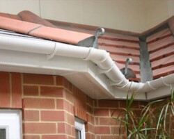 Close-up view of white PVC guttering and fascias installed along the corner of a red brick home with red interlocking ridge tiles.