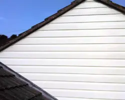 Exterior view of clean white uPVC horizontal cladding on a gable wall above a tiled residential roof against a clear blue sky.