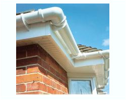 Close-up view of newly installed white uPVC fascias, vented soffits, and corner guttering system on a red brick residential property under a blue sky.