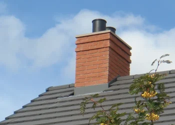 Close-up of a modern brick chimney stack with flashing and leadwork set against a grey tiled roof and blue sky