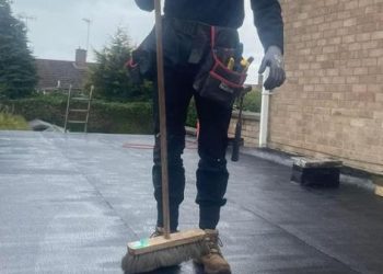 Text: Professional roofer sweeping and cleaning a newly installed flat felt roof on a residential property
