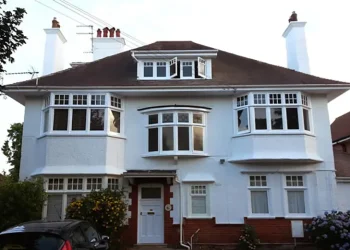 Exterior view of a large detached two-storey white rendered house with multiple bay windows, dormer roof window, and twin chimneys