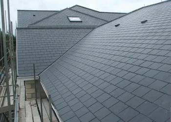 Elevated exterior view of a large pitched roof covered in grey slate tiles, featuring integrated skylights and adjacent scaffolding during construction.