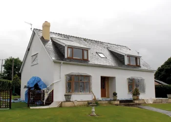 Exterior view of a detached two-storey residential house featuring a newly renovated slate roof, dormer windows, a chimney, and freshly rendered white walls during ongoing property improvements.