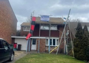 Residential house under renovation with exterior scaffolding and a debris chute setup by roofing contractors.
