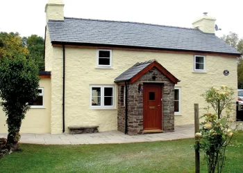Exterior view of a charming traditional cottage featuring cream-rendered stone walls, a dark slate roof, dual chimney stacks, and a stone-built entrance porch
