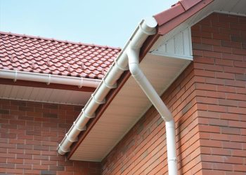 Close-up of white PVC guttering and downpipe installed on a red brick home with a red interlocking tiled roof and soffits