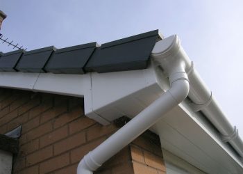 Close-up of freshly installed white uPVC guttering, downpipes, and fascias on a brick residential property with dark roof tiles.